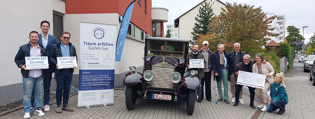 Mehrere Personen stehen fröhlich neben einem weinroten Oldtimer auf einer Straße