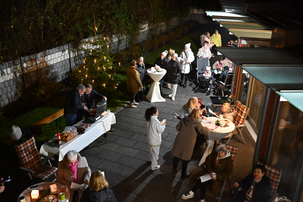 Eine Gruppe gut gelaunter Menschen feiert abends im beleuchteten Garten mit Lichtern