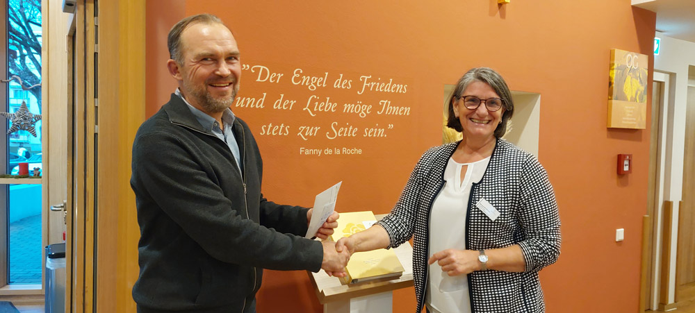 Zwei freundlich lächelnde Erwachsene geben sich in einem hellen Raum die Hand